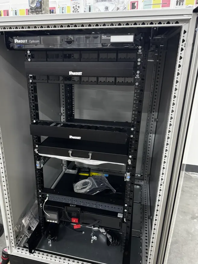 Gabinete Panduit nuevo sobre una tarima en una nave, con la charola de fibra óptica arriba y organizadores de cable