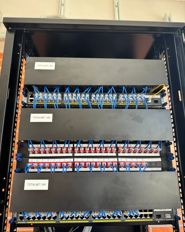 Rack de piso instalado por Totalnet, con tres organizadores de cable rotulados TOTALNET.MX, paneles de conectores rojos y patch cords azules